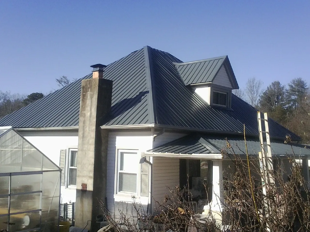 Dark blue standing seam metal roof on a white farmhouse with dormer — Slate & Tile Roof Repair by Roofing Brothers in Lakehurst