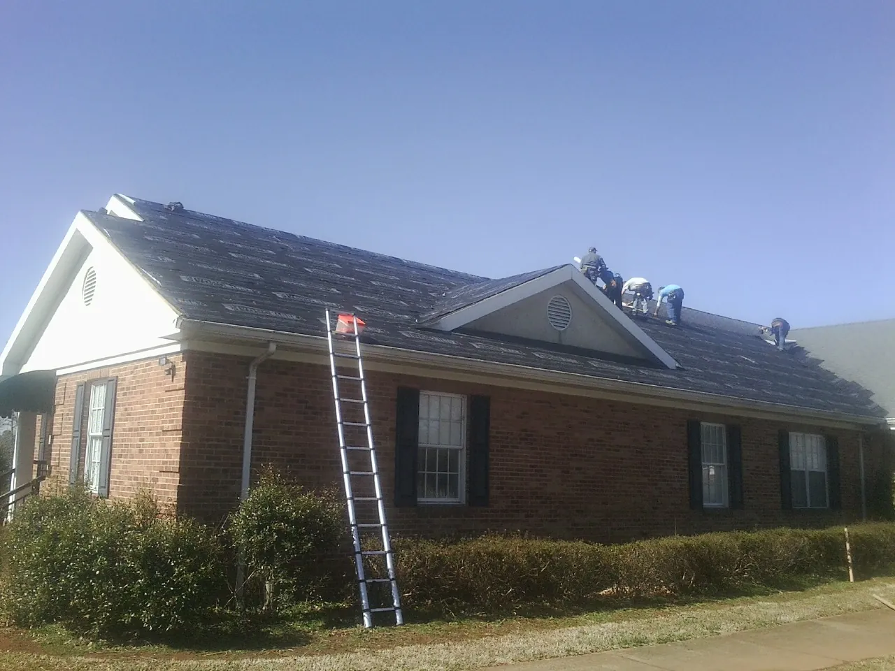 Crew tearing shingles off a brick ranch roof with a ladder set — Emergency Roof Repair work by our crew in Lakehurst