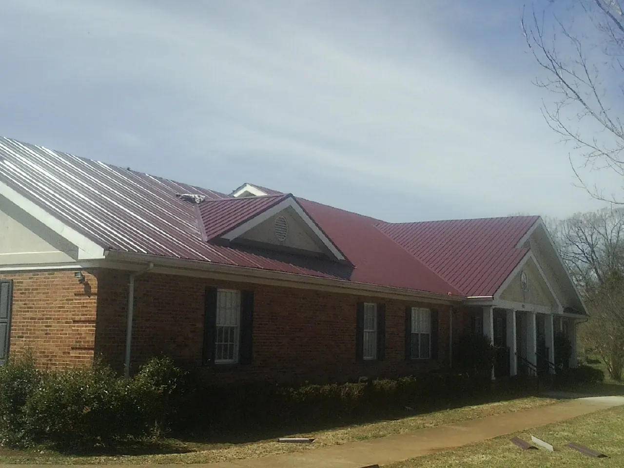 Red metal roof with gabled entries on a long brick building, from a Hail Damage Roof Repair job in Lakehurst