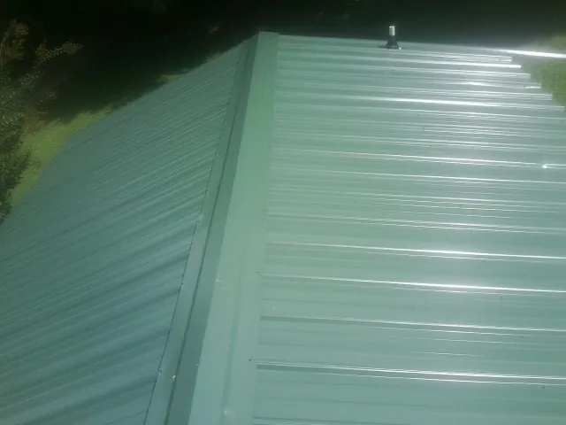 New green metal panels meeting at the ridge of a roof — Flat Roof Repair work by our crew in Lakehurst