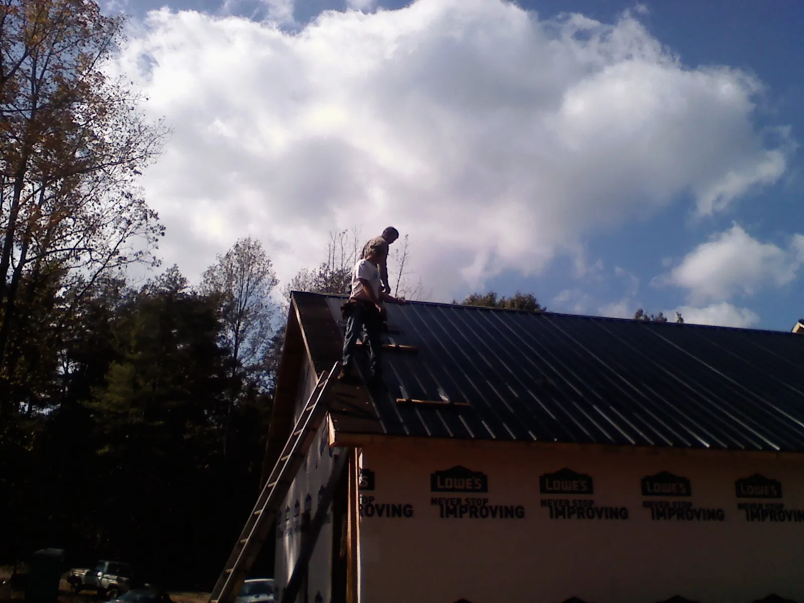 Roofer fastening dark metal panels high against a cloudy sky, from a Roof Inspection job in Lakehurst