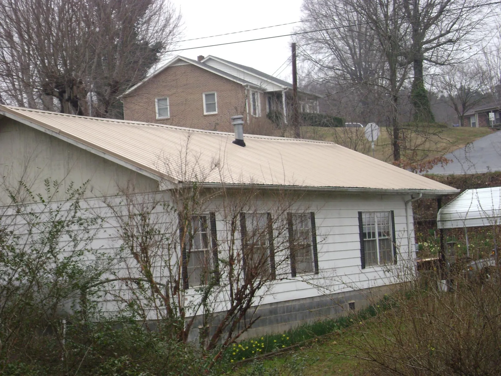 Tan metal roof on a white sided house set into a hillside — Commercial Roofing by Roofing Brothers in Lakehurst